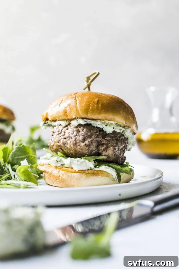 Delicious lamb burgers topped with a generous dollop of pesto whipped feta, served on buns, creating a gourmet Mediterranean-inspired meal.