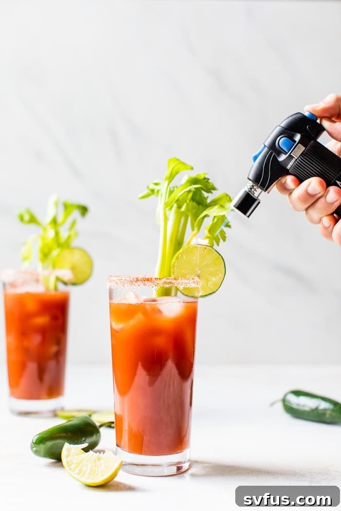 Two Skinny Bloody Mary cocktails with torched lime garnish, viewed from above, with fresh ingredients in the background.