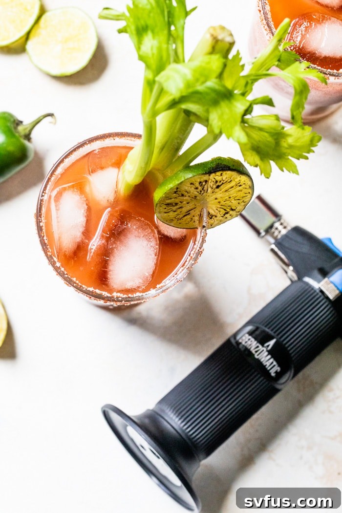 A hand holding a torched lime slice above a Skinny Bloody Mary cocktail.