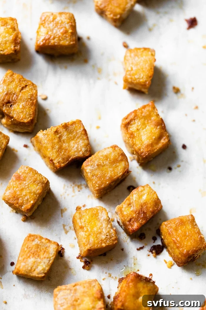 Golden brown crispy baked tofu cubes arranged neatly on a parchment-lined baking sheet, ready to be served or added to a dish. The texture is visibly crunchy and inviting.