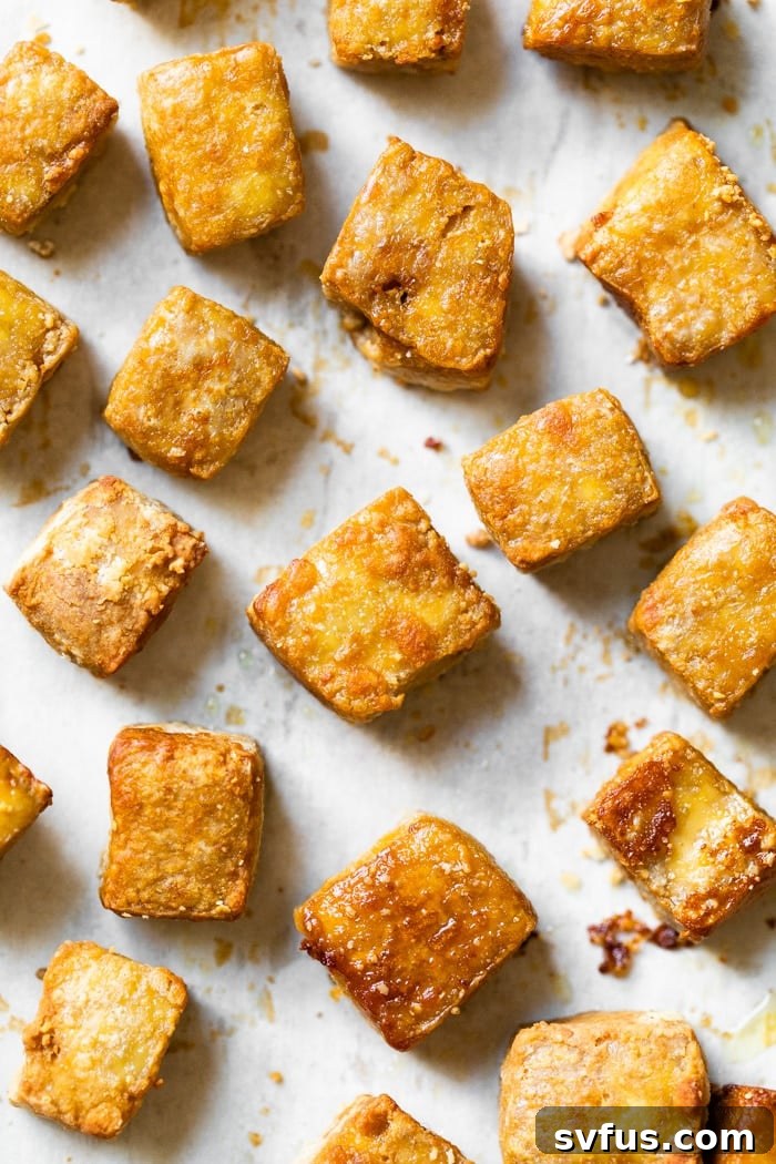 Crispy baked tofu cubes, perfectly golden brown and crunchy, spread out on a parchment-lined baking sheet, glistening with savory flavor.