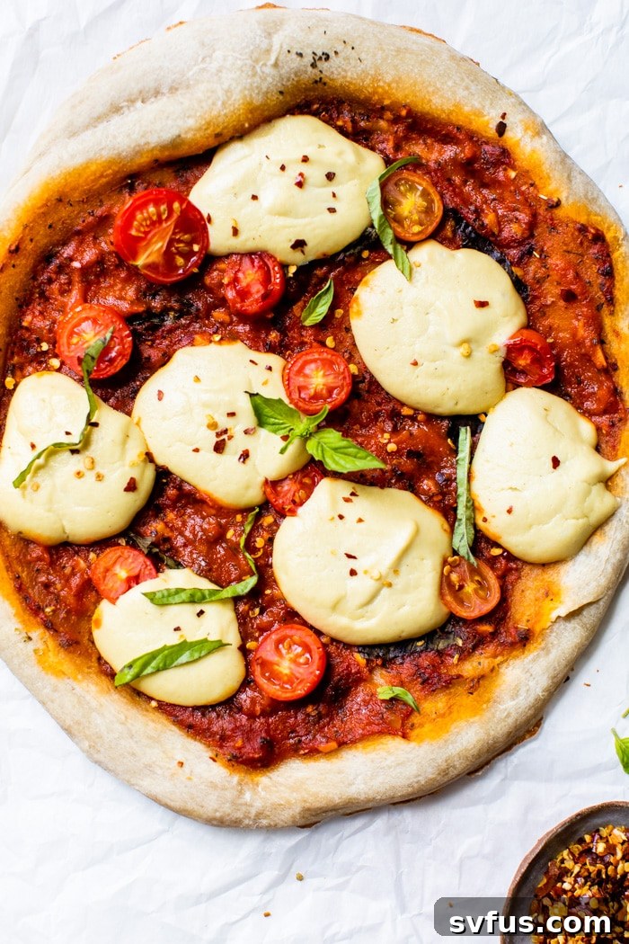 Close-up of a freshly baked vegan pizza on parchment paper, highlighting melted cheese and crisp crust.