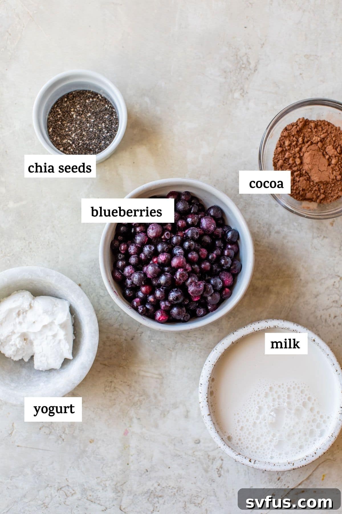 Fresh ingredients laid out on a kitchen counter, including vibrant frozen blueberries, rich cocoa powder, and creamy yogurt, awaiting their transformation into a delicious smoothie.