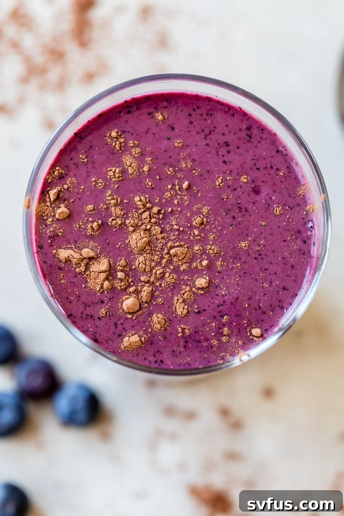 A close-up shot of a rich, purple-colored chocolate blueberry smoothie, beautifully presented in a clear glass and topped with a delicate dusting of cocoa powder, inviting a refreshing sip.