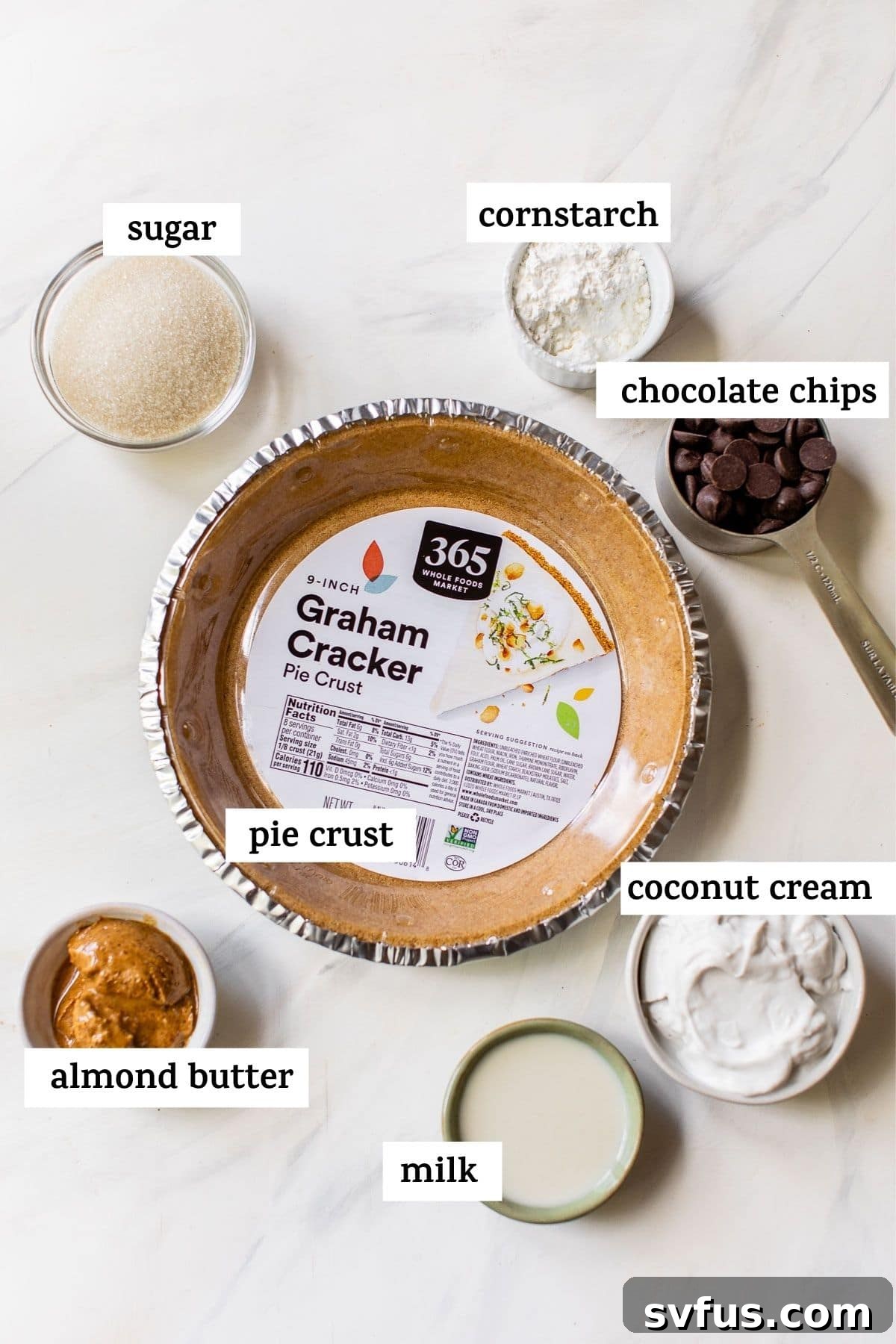 A selection of ingredients for no-bake chocolate pie laid out on a table, including chocolate chips, coconut cream, almond butter, and a pie crust.