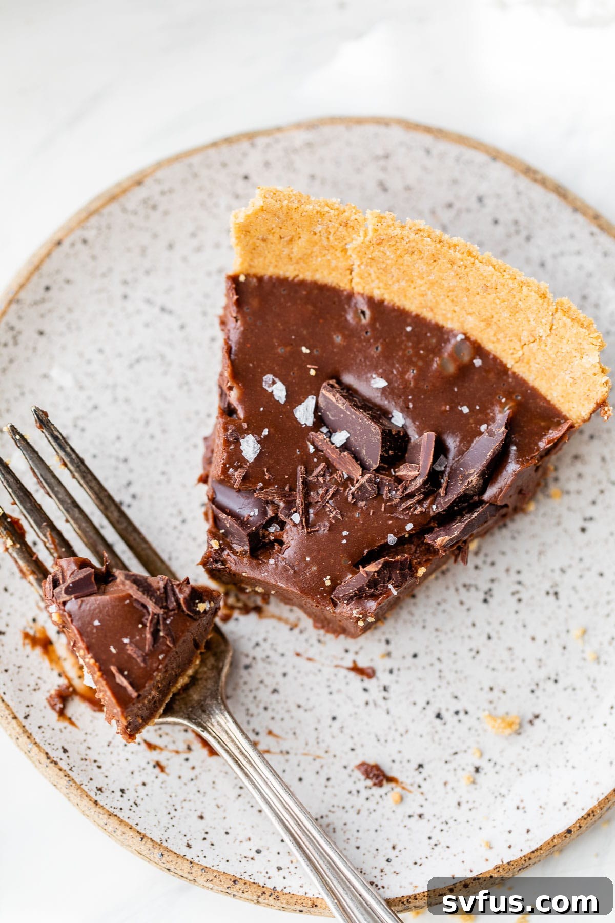 A close-up of a slice of no-bake chocolate pie on a plate with a bite taken out, showing the creamy filling and crisp crust.