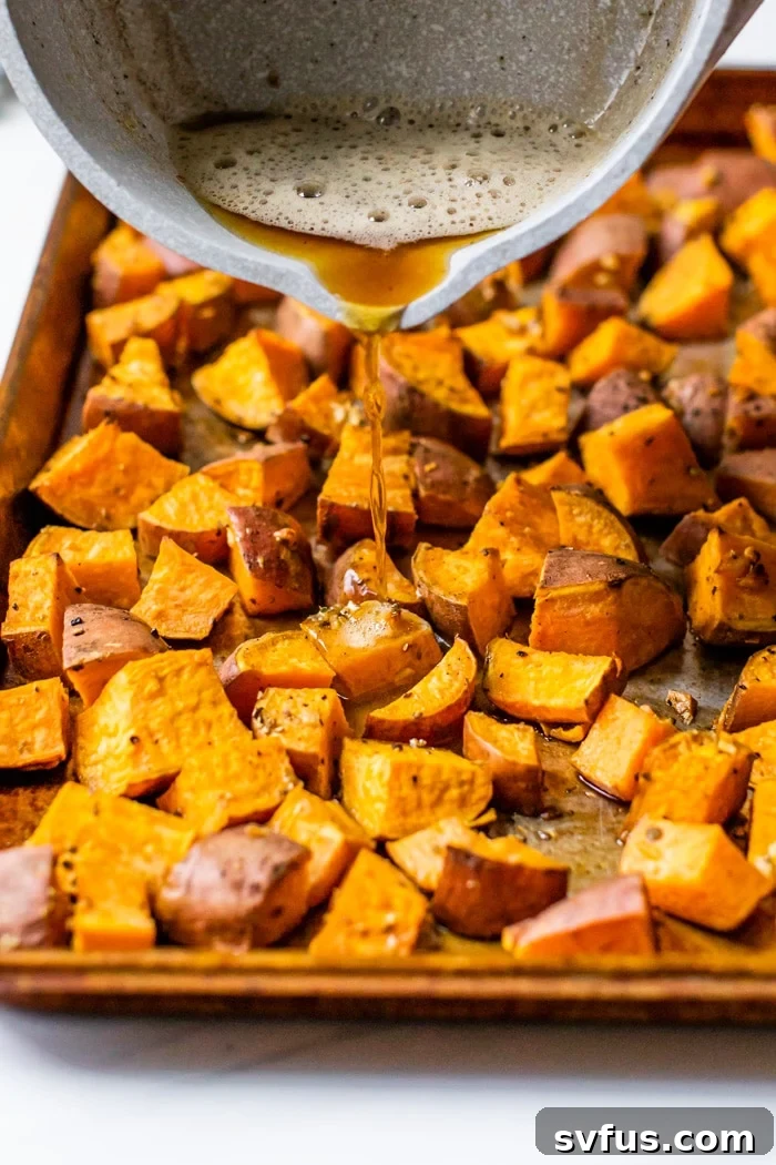 A close-up of browned butter being poured over a baking sheet full of roasted sweet potatoes