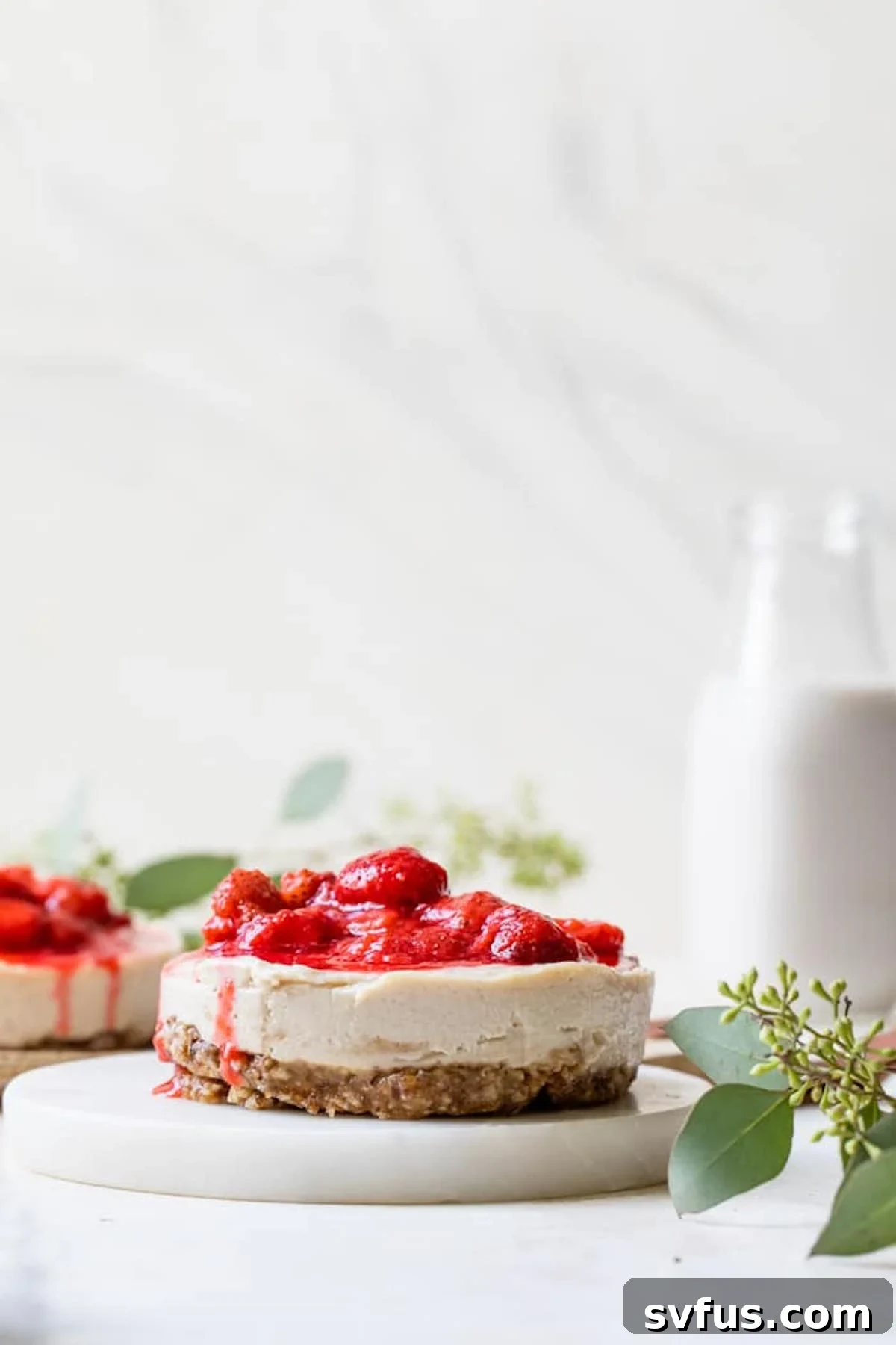 Creamy cashew vegan cheesecake topped with fresh strawberries on a white background, highlighting its no-bake simplicity and vibrant fruit topping.