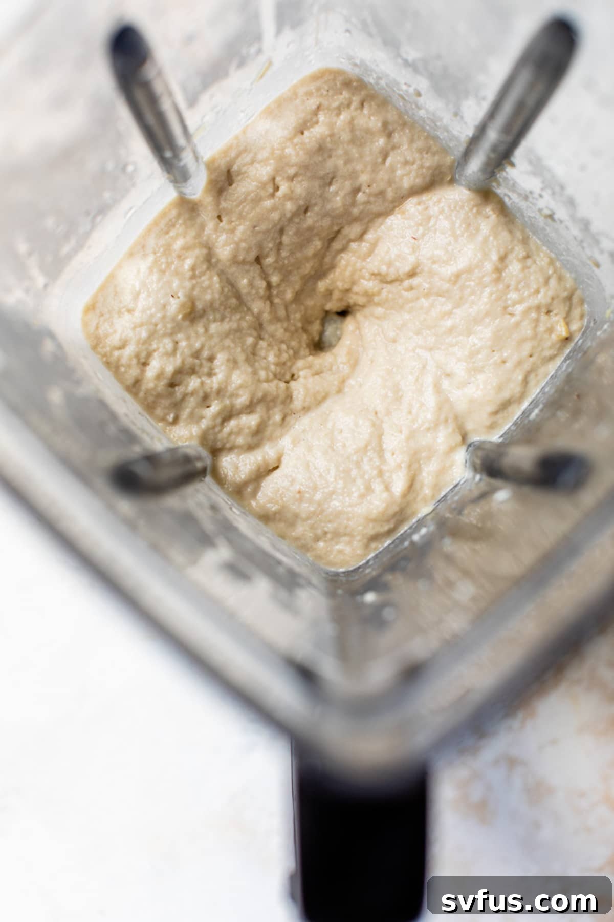 Close-up of a blender filled with creamy, blended cashews, forming the base for the vegan cheesecake filling.