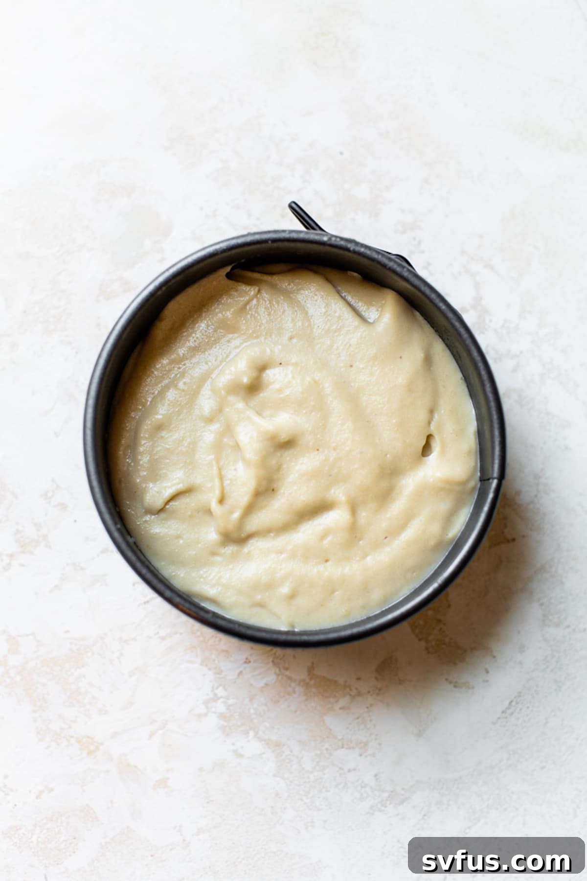 A vegan cheesecake with a light-colored filling, ready to be chilled in a round springform pan.