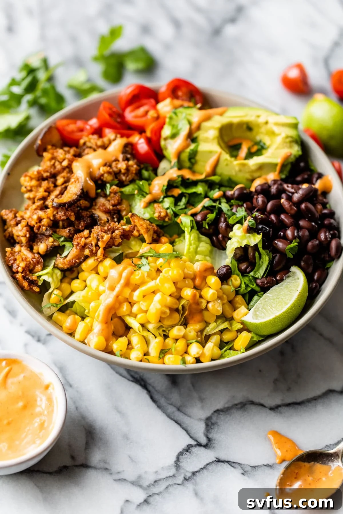 A close-up view of a vibrant vegan taco salad served in a clear bowl, showcasing the colorful layers of fresh romaine, black beans, corn kernels, diced tomatoes, and a generous portion of savory walnut taco meat, all ready to be drizzled with dressing.