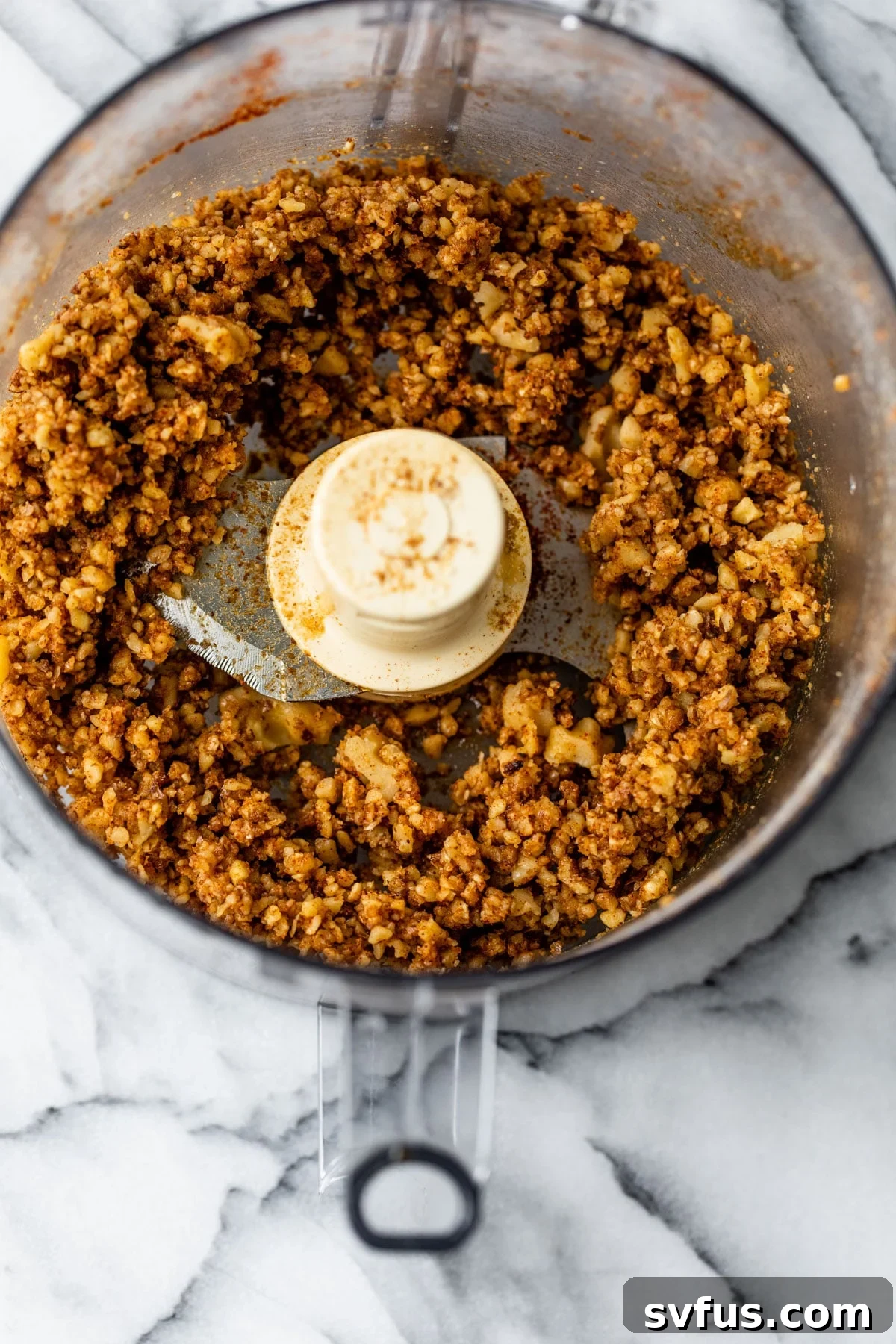 A food processor containing seasoned crushed walnuts, illustrating the preparation stage of the walnut taco meat, with visible spices mixed into the finely textured nuts, ready for cooking.