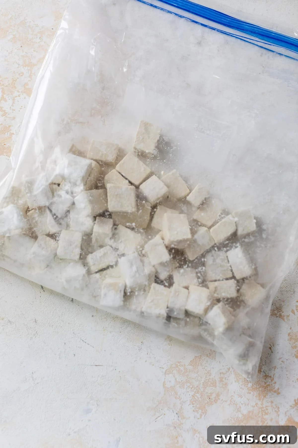 Close-up image of tofu cubes being tossed with cornstarch in a large ziplock bag, illustrating the coating process.