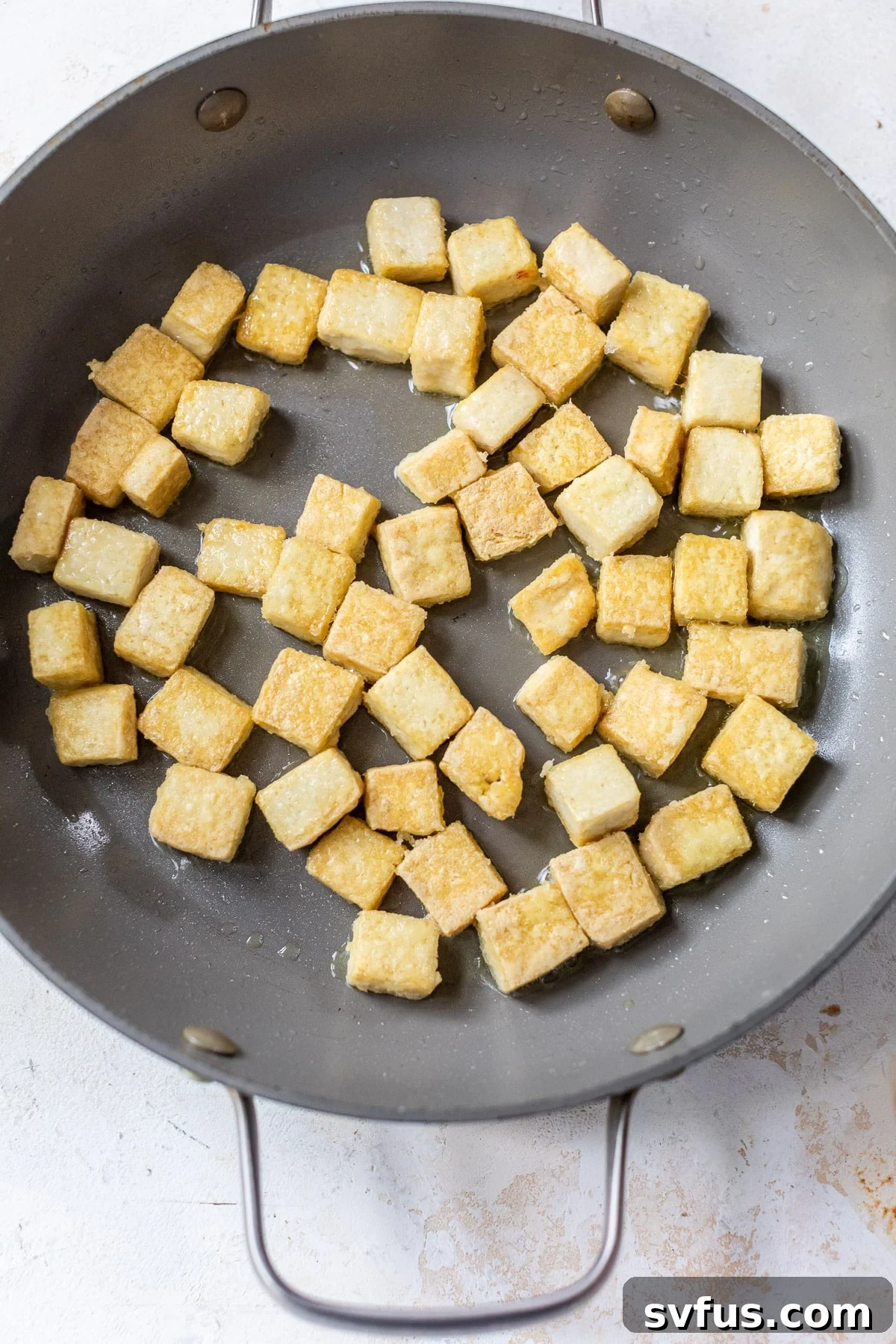 Crispy golden tofu cubes frying in a large grey skillet, demonstrating the desired color and texture.
