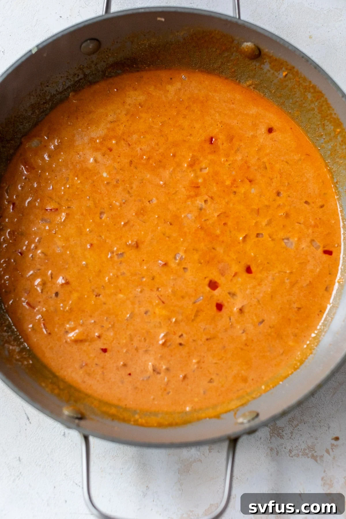 A vibrant red curry sauce simmering in a large grey skillet, indicating its creamy texture and rich color.