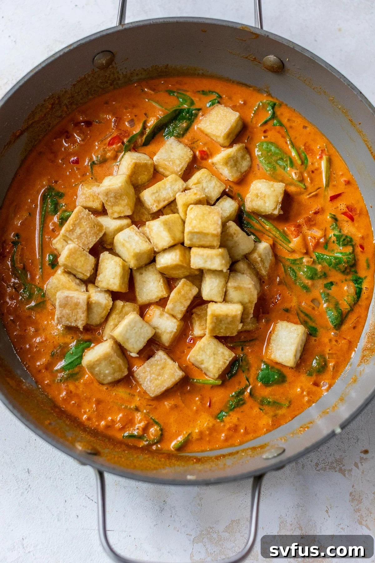 A large grey skillet filled with crispy golden-brown tofu cubes immersed in a rich red curry sauce, ready to be served.