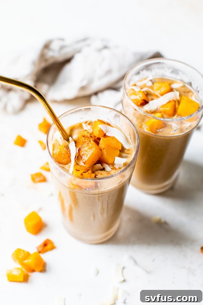 Vibrant butternut squash smoothie in a clear glass, garnished with a sprinkle of cinnamon, sitting on a wooden surface.
