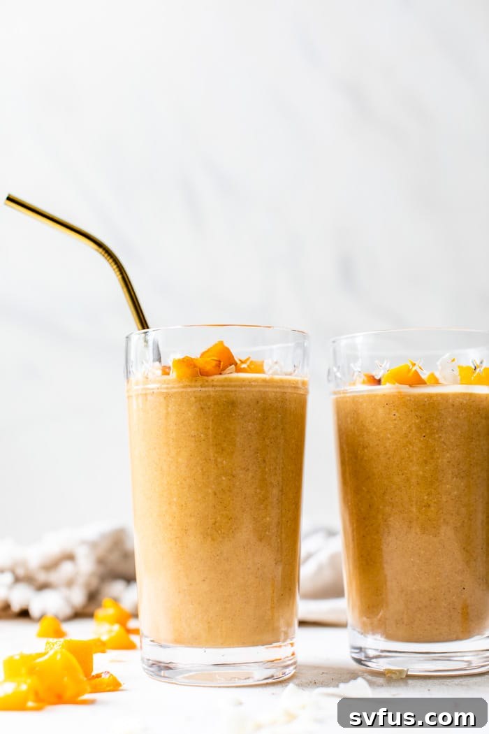 Butternut squash smoothie in a clear glass with a straw, placed on a light-colored surface, inviting to drink.