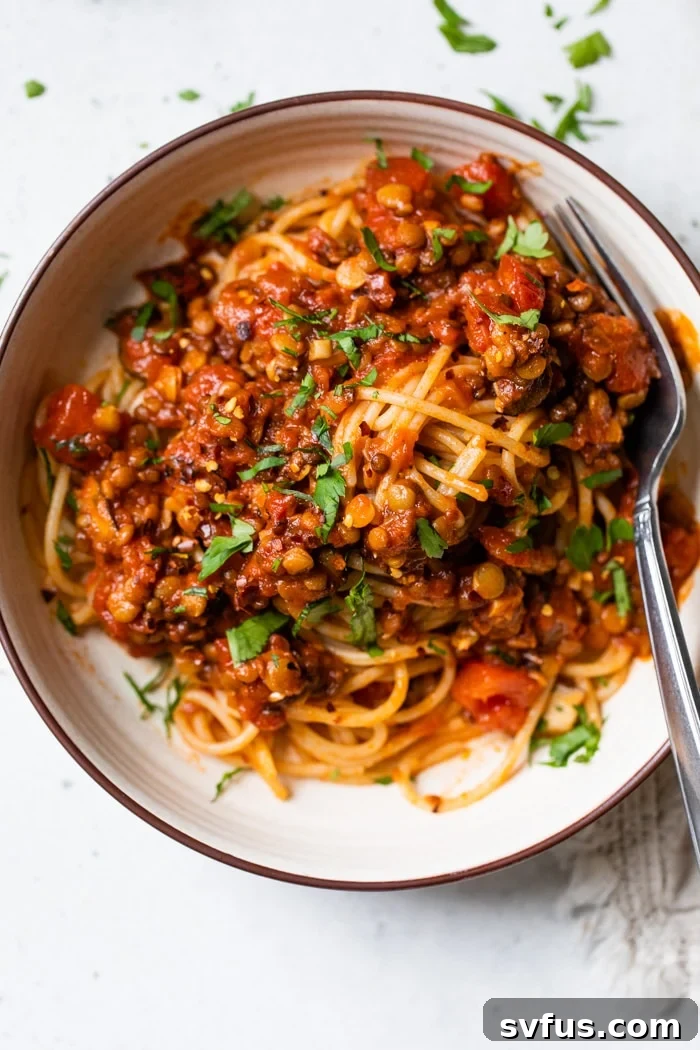 A vibrant bowl of pasta topped with rich red lentil bolognese sauce, garnished with fresh basil.