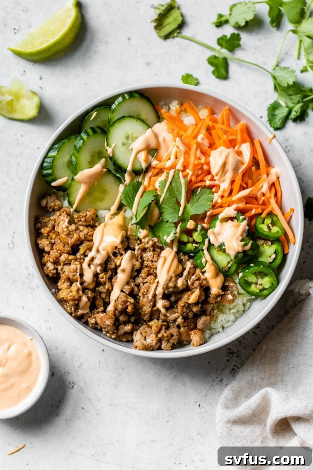 Close-up of a vibrant Banh Mi Bowl, showcasing the seasoned ground pork, fresh cucumber, shredded carrots, and a drizzle of sriracha mayo over cauliflower rice. Garnished with fresh cilantro.