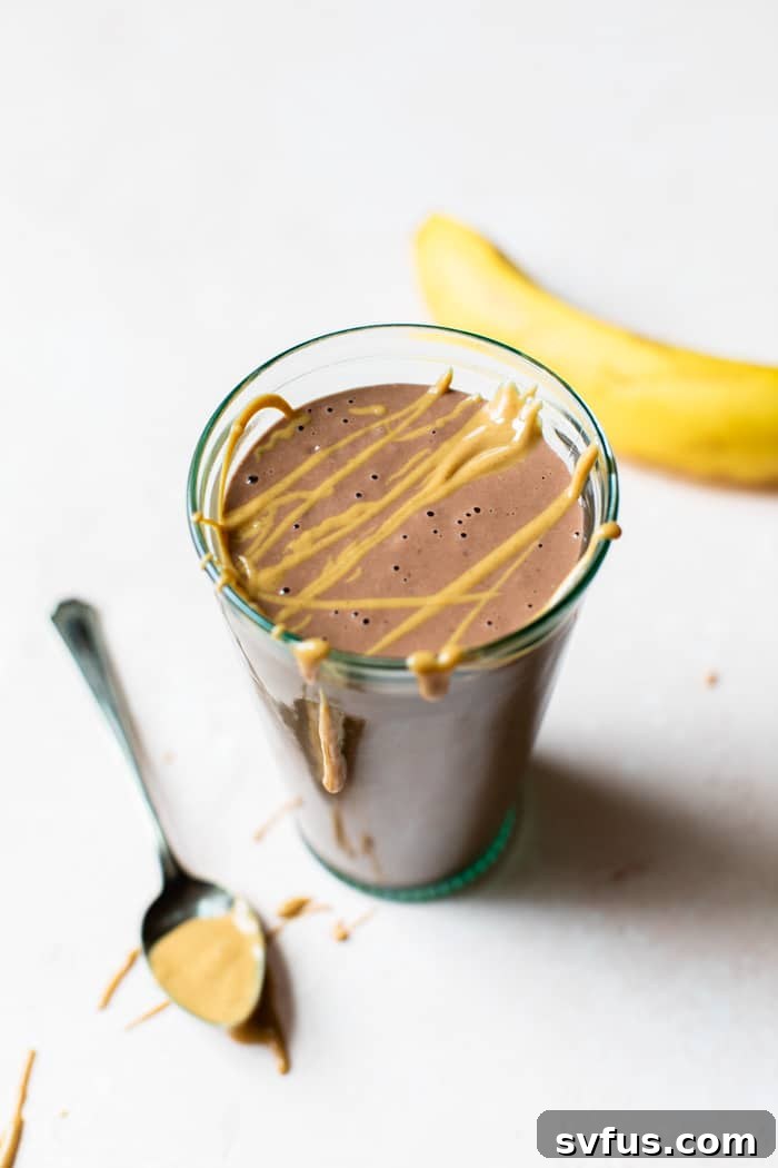 A tempting Chocolate Peanut Butter Protein Smoothie in a glass, elegantly drizzled with nut butter on top. Made with healthy ingredients, this smoothie tastes like a dessert in a glass and is perfect as a post-workout drink or a quick breakfast option.