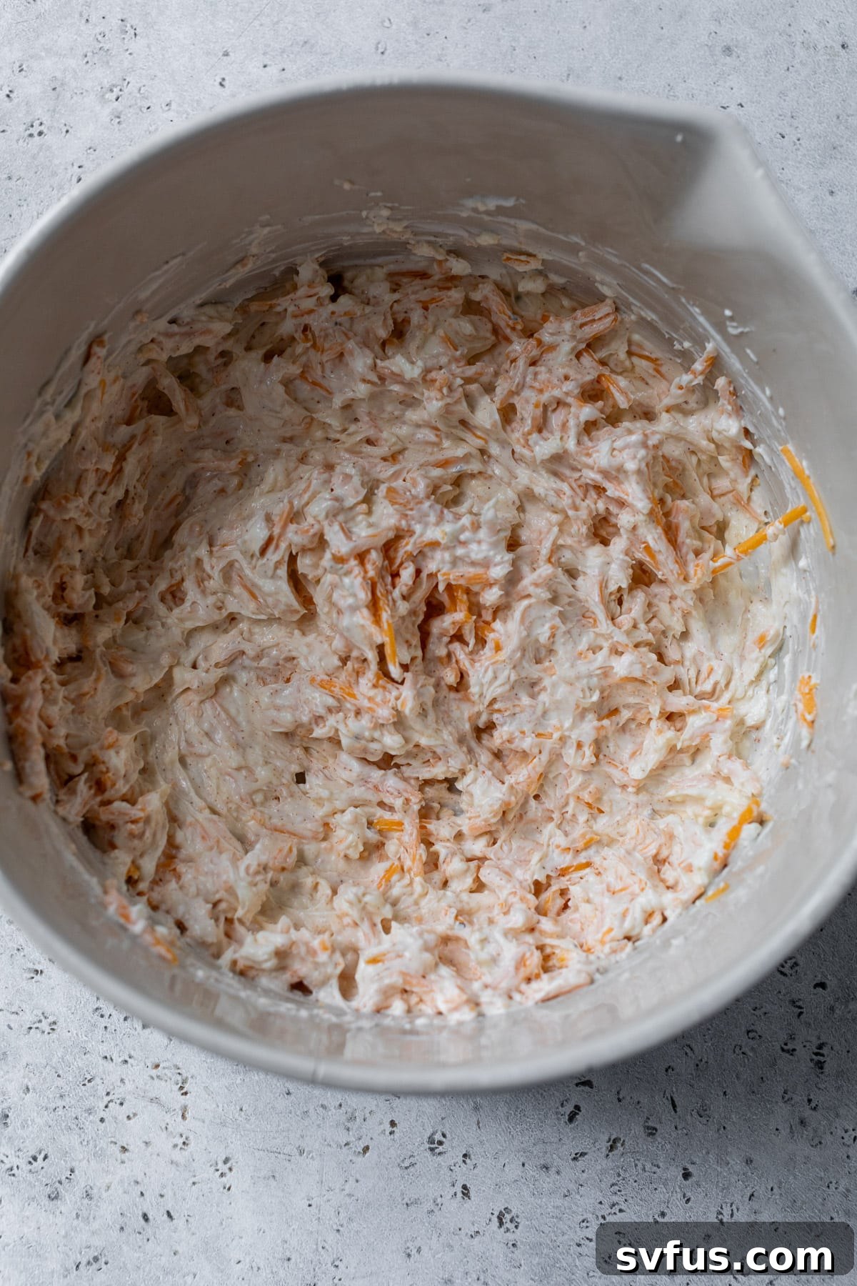 Close-up of uncooked hot crab dip mixture in a large mixing bowl, showing the creamy base and crab pieces.