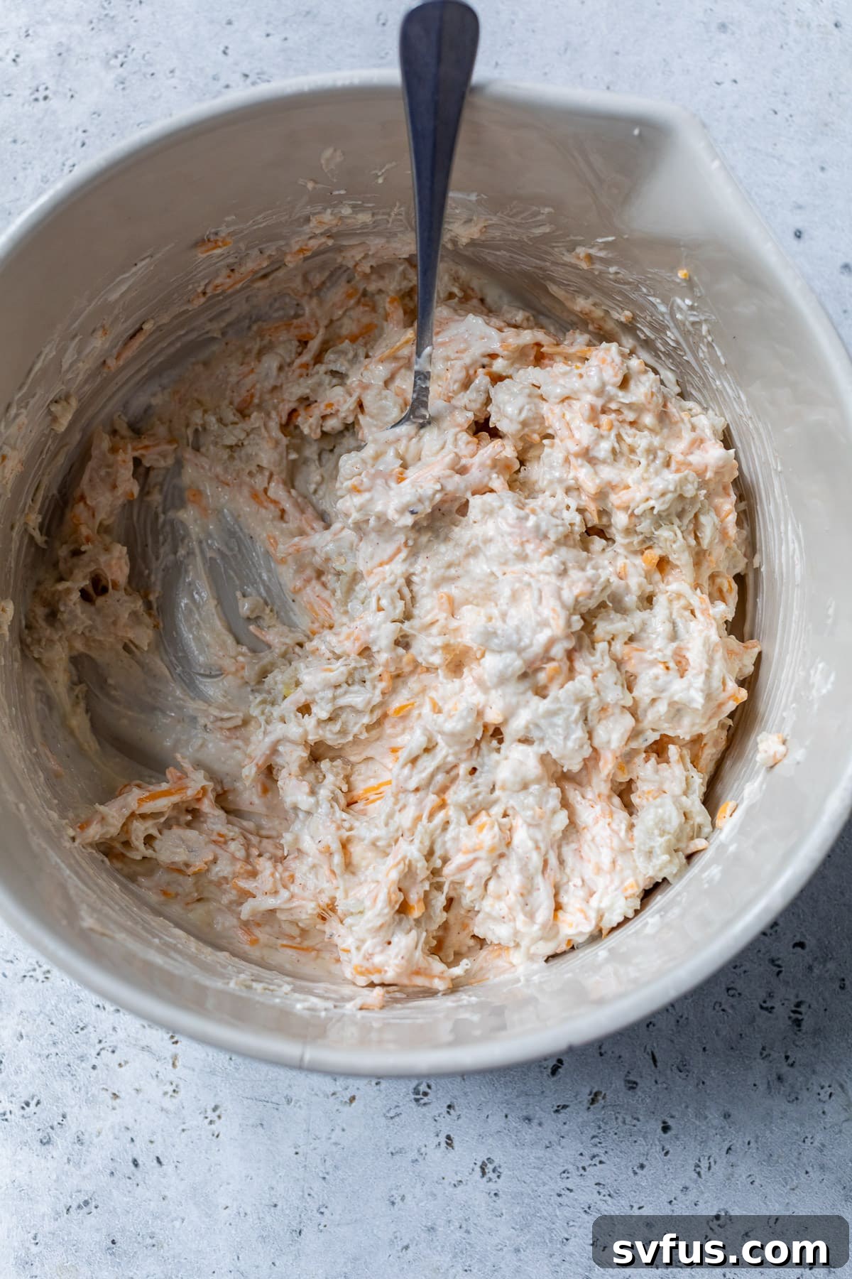 A rubber spatula mixing creamy crab dip with shredded cheese in a large bowl, showcasing the combined texture.