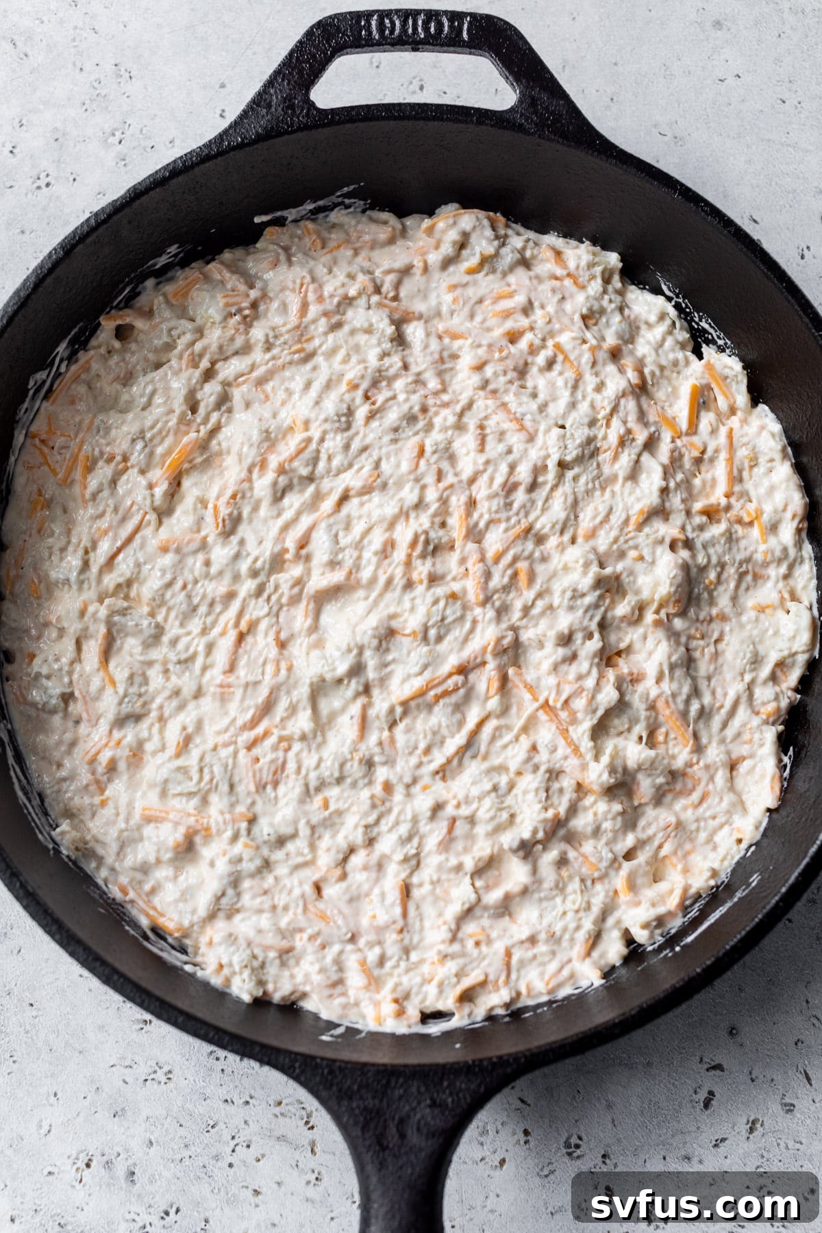 Assembling cheesy crab dip mixture in a large black skillet before baking, with a generous layer of shredded cheese on top.