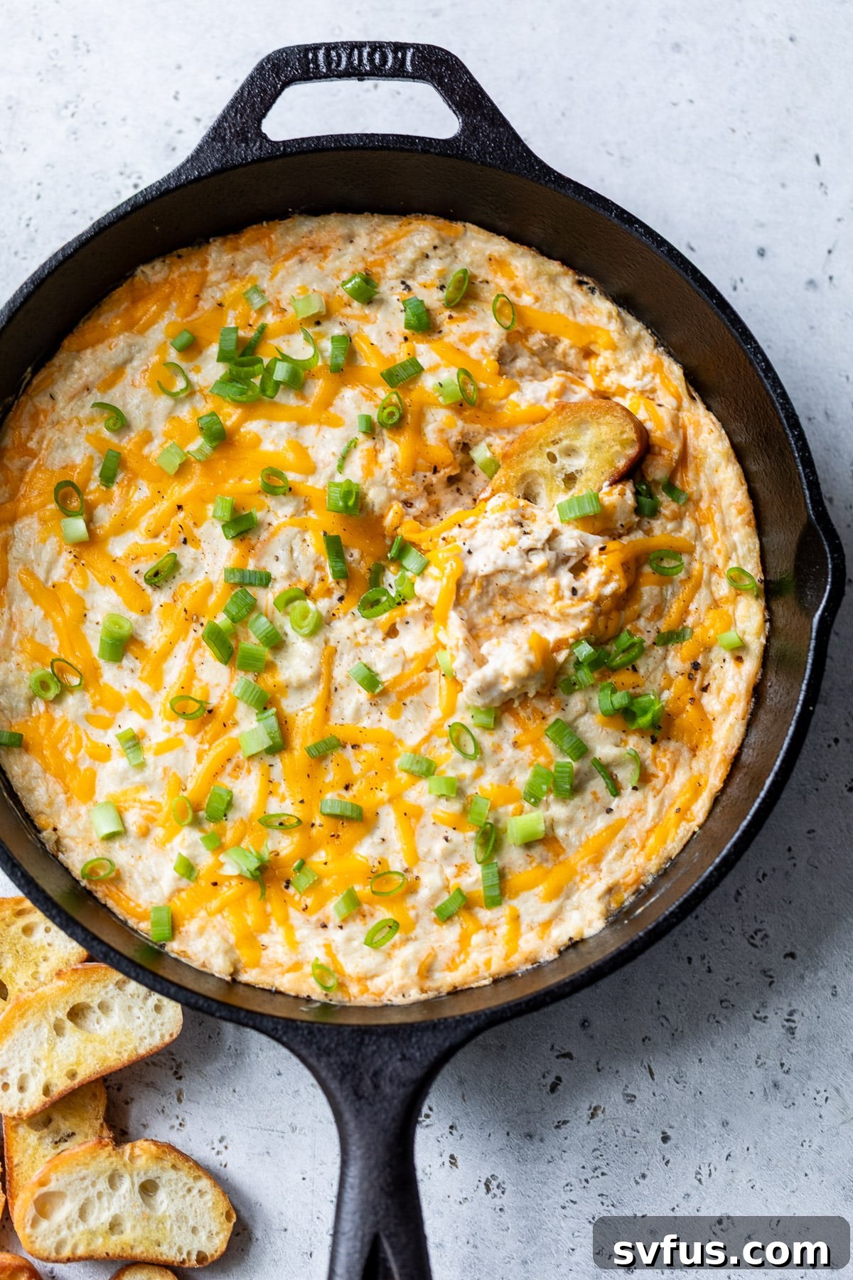 A close-up shot of hot crab dip in a skillet, bubbling and golden brown, with a baguette slice ready for dipping.