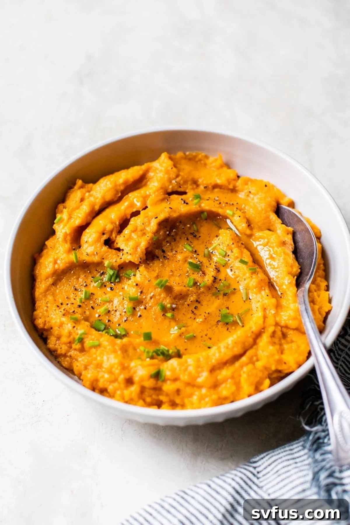 A large bowl brimming with fluffy and creamy savory mashed sweet potatoes, garnished with fresh chives, ready to be served.