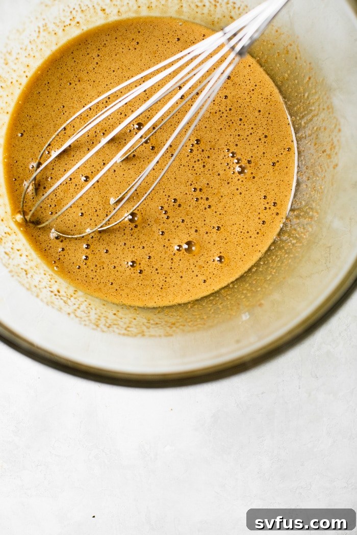 A bowl showcasing whisked eggs and coconut sugar, appearing light and frothy, a crucial step for crackly-top brownies