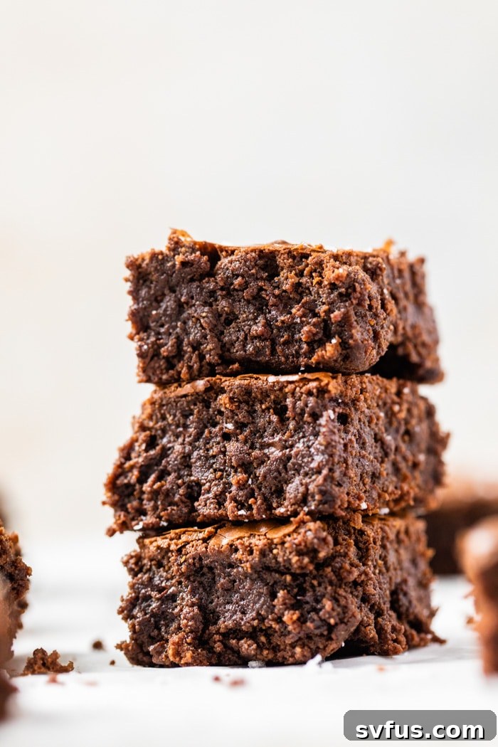 A perfectly stacked pile of freshly baked paleo brownies, showcasing their crackly tops and rich, dark interior