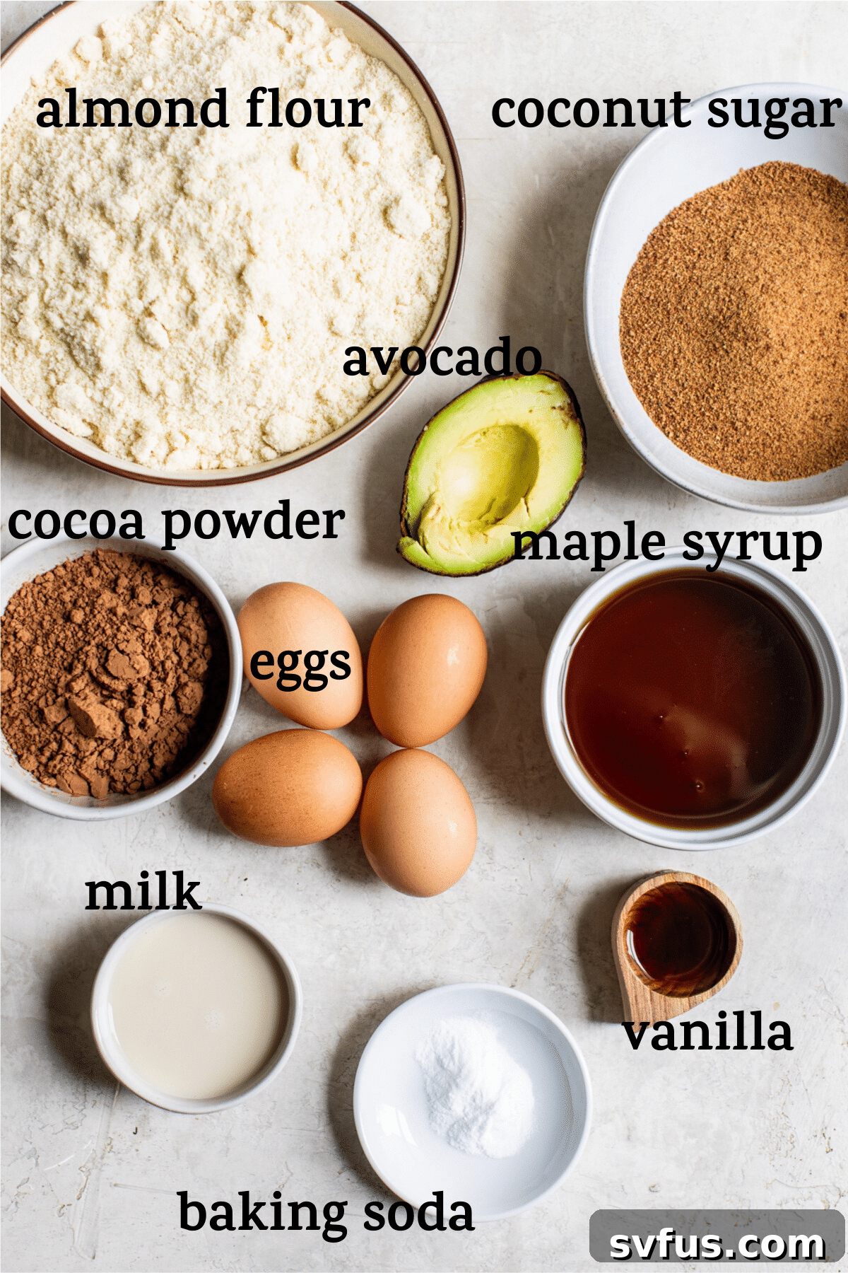 Assorted baking ingredients for chocolate avocado cake laid out, including mashed avocado, almond flour, and cocoa powder.