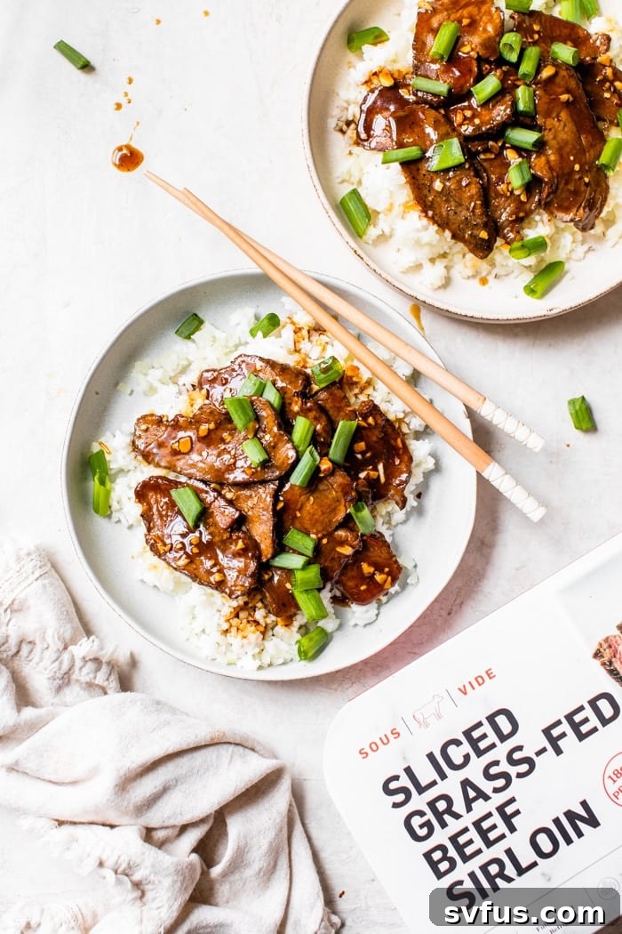 Healthy Mongolian Beef served in a white bowl over rice, garnished with fresh green onions.