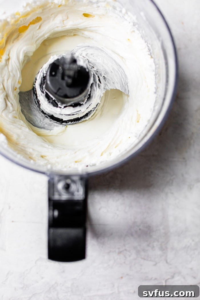 Softened goat cheese and cream cheese in a food processor, ready to be whipped into a creamy dip.