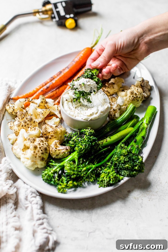 A beautifully presented platter of charred broccolini, carrots, and cauliflower with a side of garlic whipped goat cheese dip, ready to be enjoyed.
