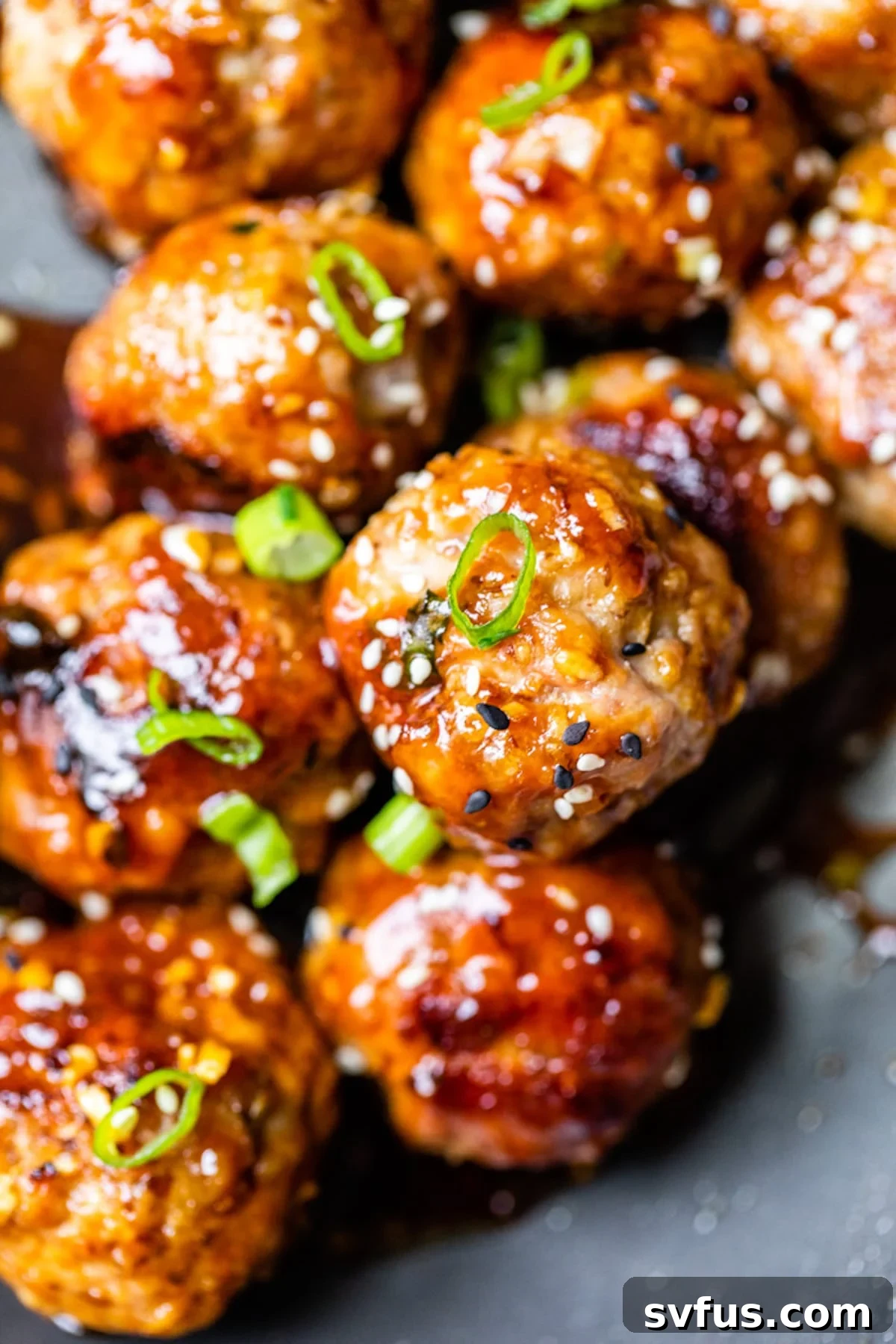 Close-up of sticky teriyaki pork meatballs garnished with sesame seeds and chopped green onions.