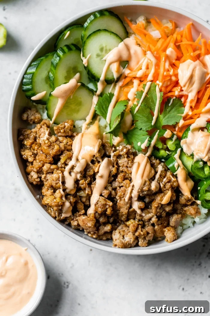 A delicious Banh Mi Bowl featuring seasoned ground pork, crisp carrots, refreshing cucumber, and a drizzle of sriracha mayo, suitable for paleo and Whole30 diets.