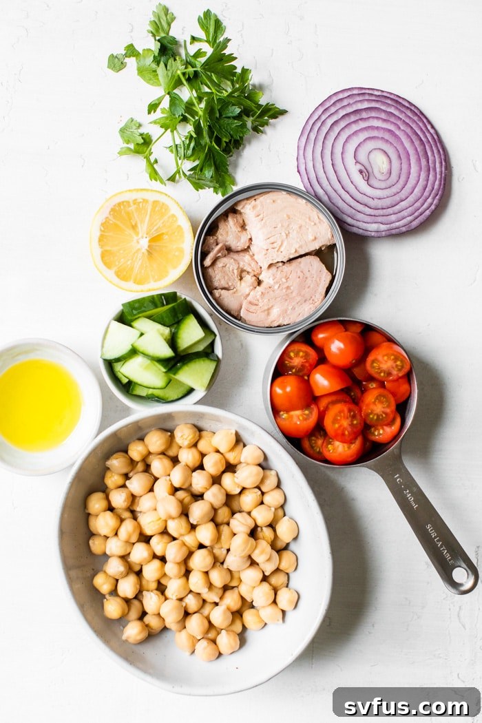 A beautiful arrangement of key ingredients for Mediterranean Chickpea Tuna Salad, including canned tuna, chickpeas, grape tomatoes, cucumber, red onion, lemon, and fresh parsley, all ready for preparation.