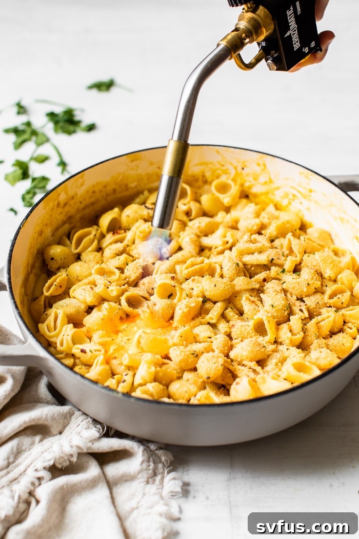 Vegan mac and cheese being charred with a kitchen torch for a crispy topping