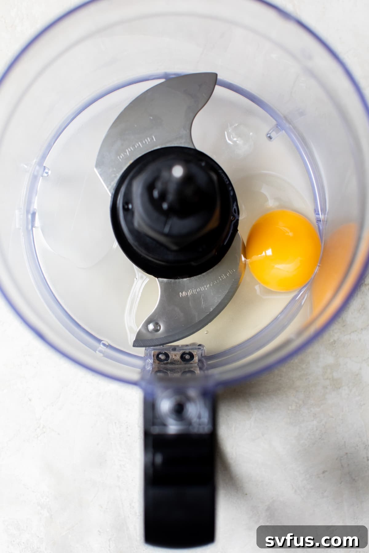 A single egg in the bottom of a food processor bowl, ready to be pulsed.