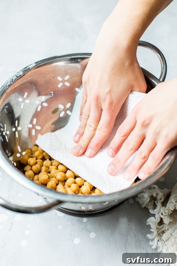 Rinsed chickpeas draining in a colander under running water, showing the importance of preparing them for roasting.