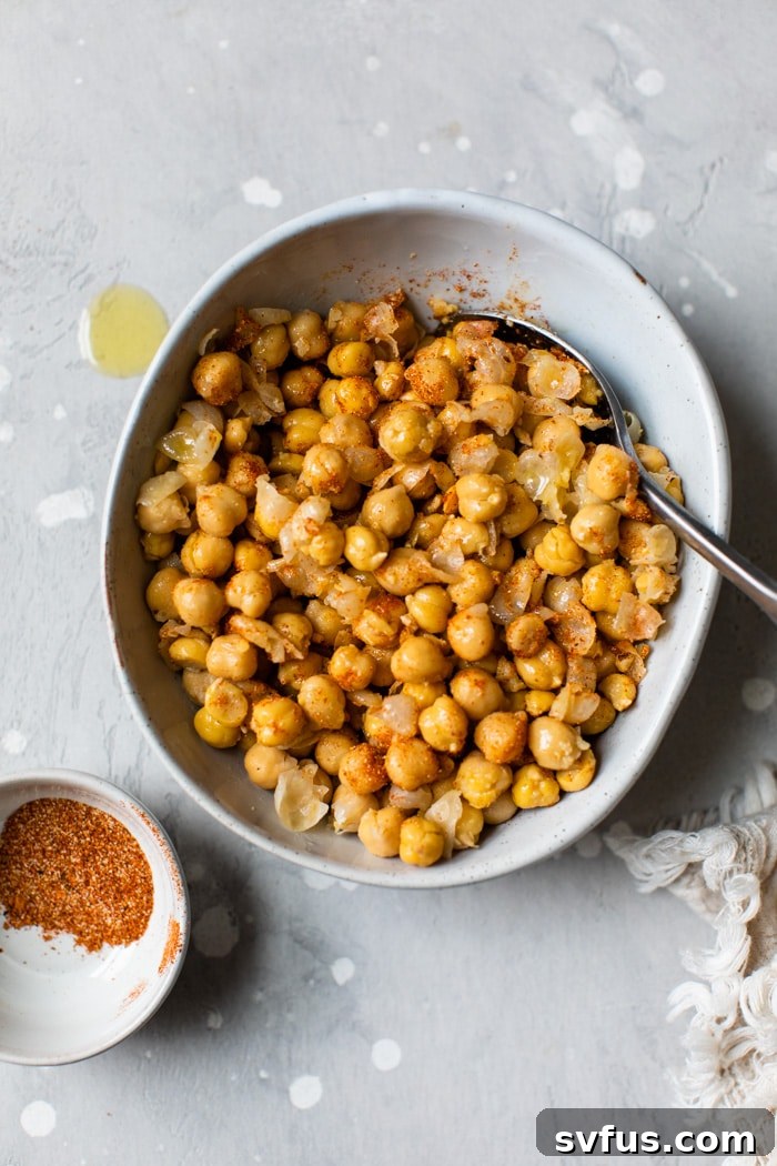 Chickpeas in a mixing bowl, generously coated with olive oil and cajun seasoning, ready for roasting.