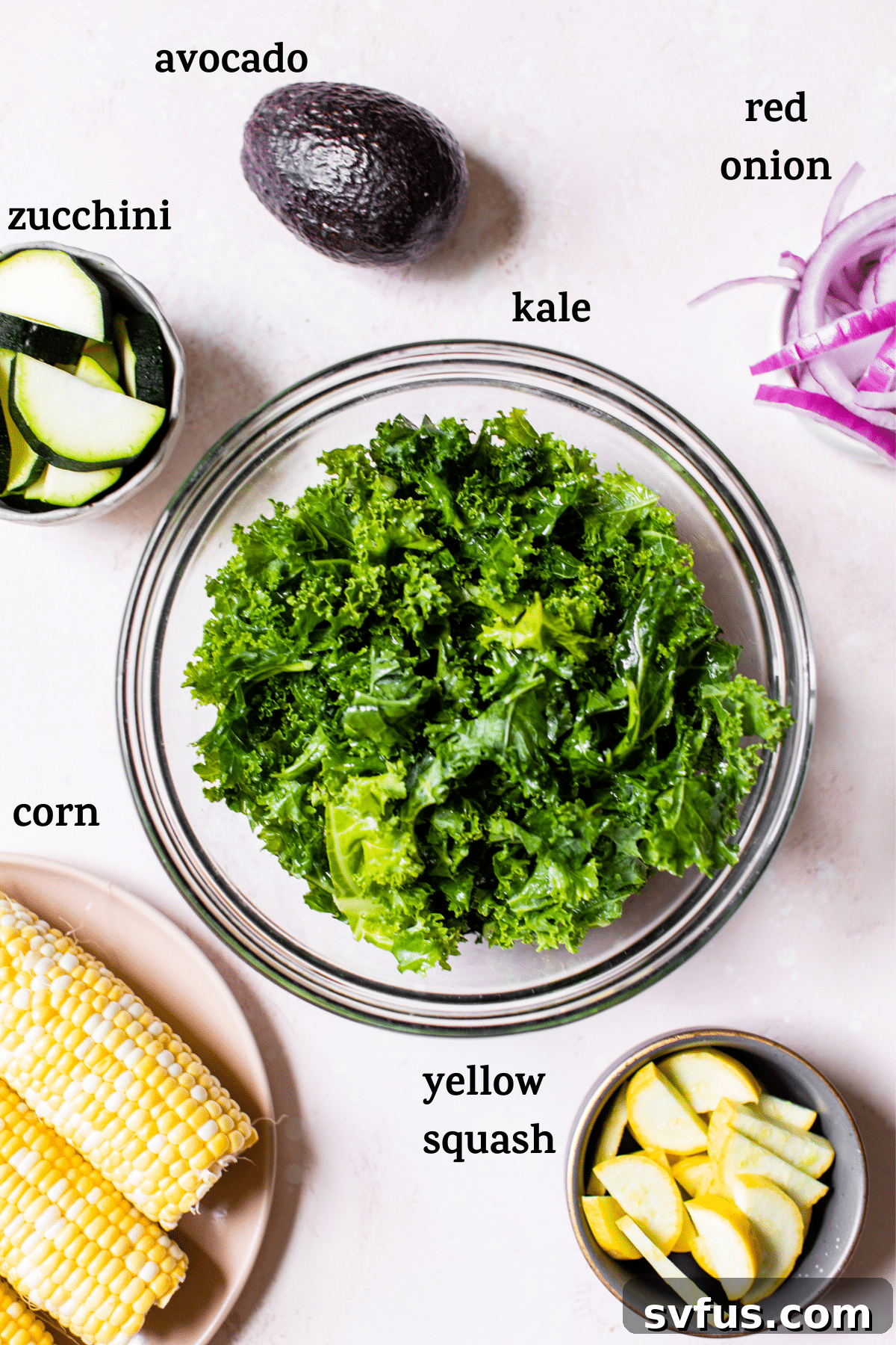 A flat lay of fresh ingredients including kale, corn on the cob, zucchini, yellow squash, red onion, avocado, jalapeño, and lime, ready for the grilled corn kale salad.