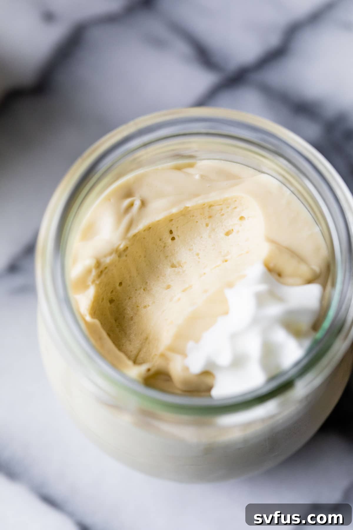 A single jar of light and airy mango mousse, elegantly topped with a swirl of vegan whipped cream and a mint leaf, signaling a delightful dessert experience.