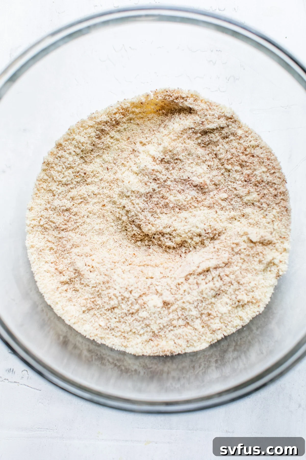 A bowl filled with blanched almond flour, cinnamon, baking soda, and salt, ready to be combined for the muffin batter