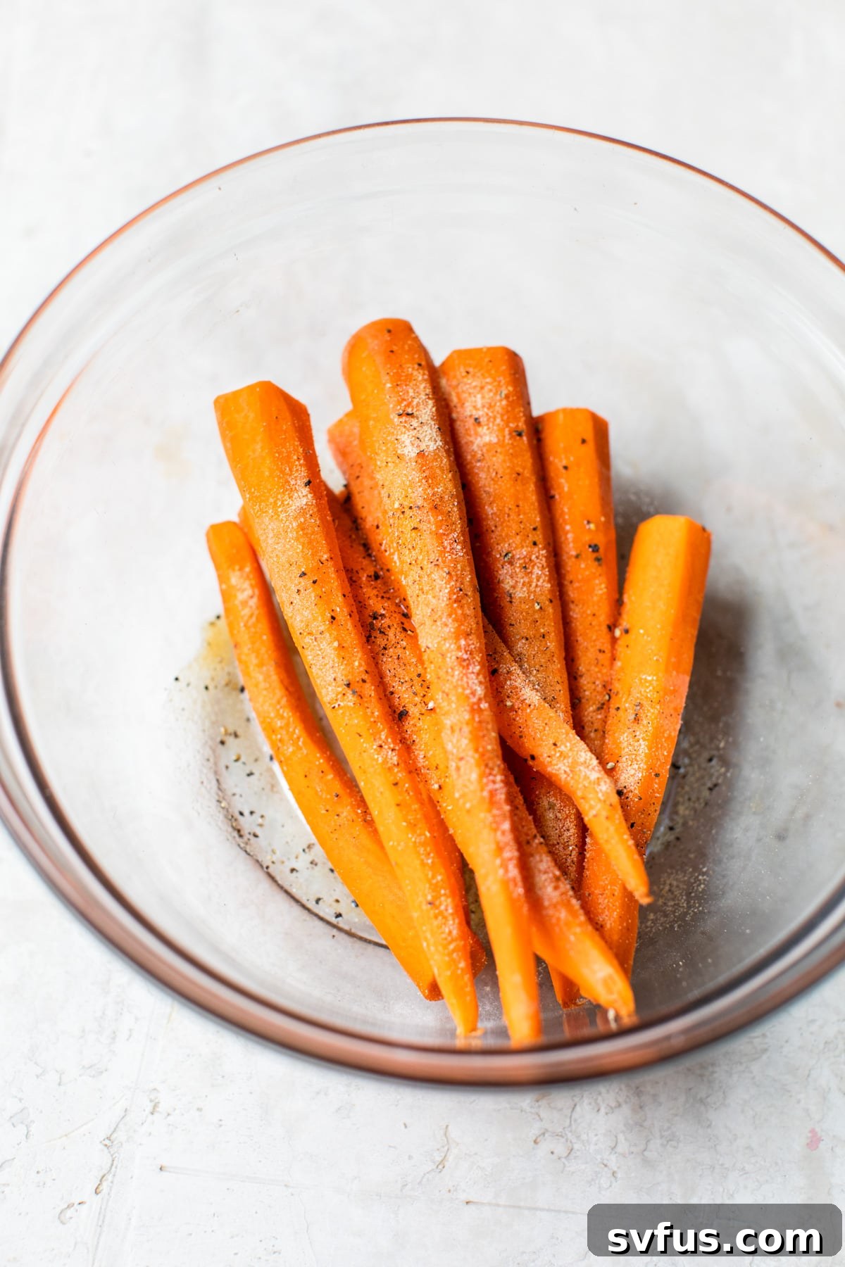 A bowl of freshly peeled and chopped raw carrots, ready for seasoning.