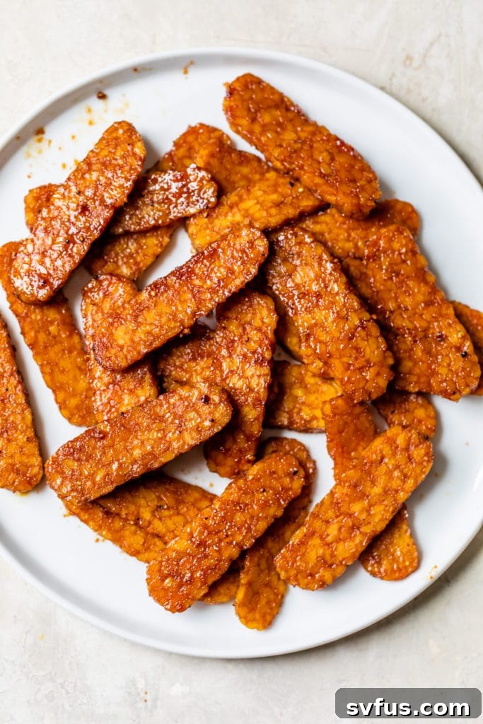 Sliced tempeh bacon on a plate, garnished with fresh herbs, ready to serve.