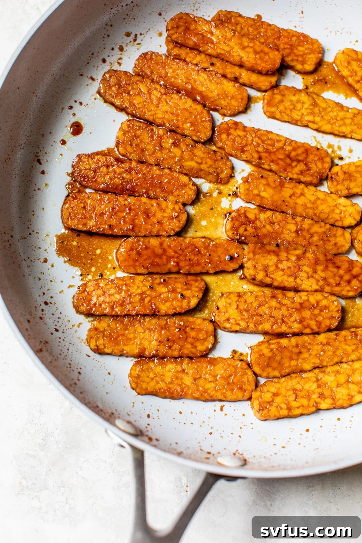 Tempeh strips simmering in a rich, dark marinade in a skillet on the stove.