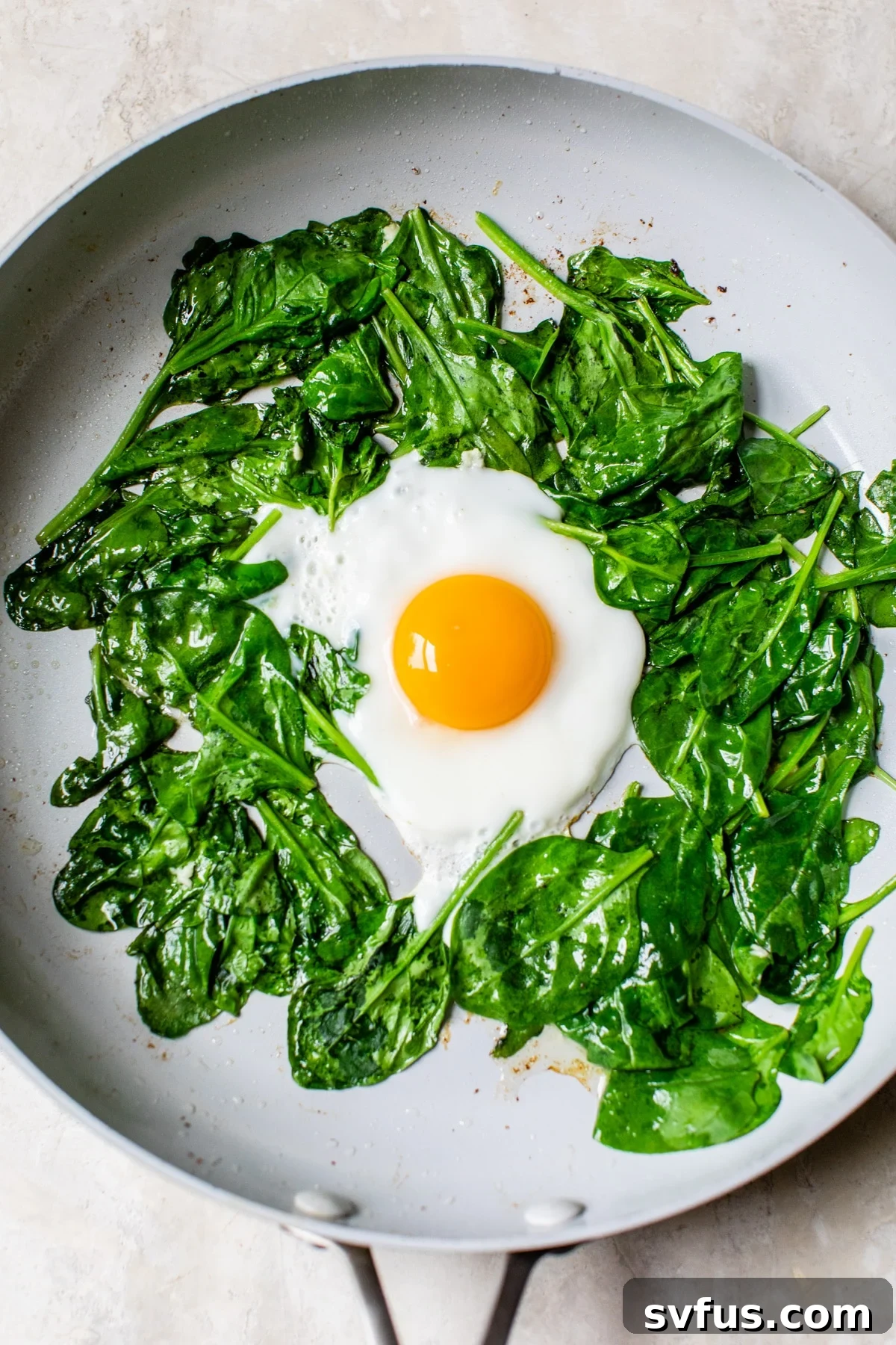 Spinach wilting and an egg frying in a hot skillet, ready to be added to the sweet potato bowl.